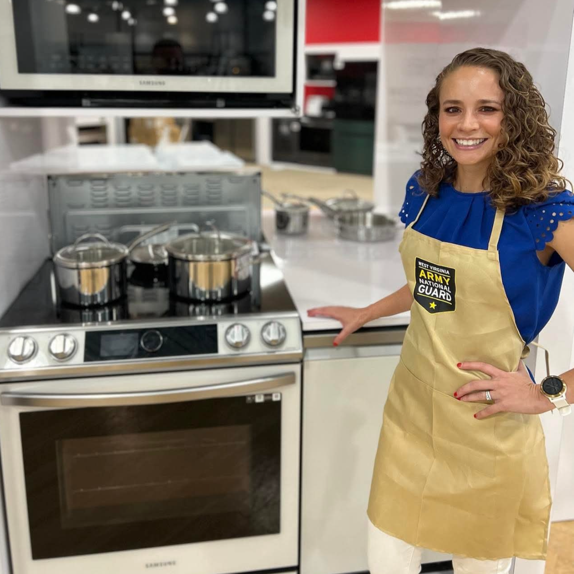 WVNG Dietitian Shari Wright Pettit stands an oven, smiling at the camera and wearing a WV Army National Guard apron.